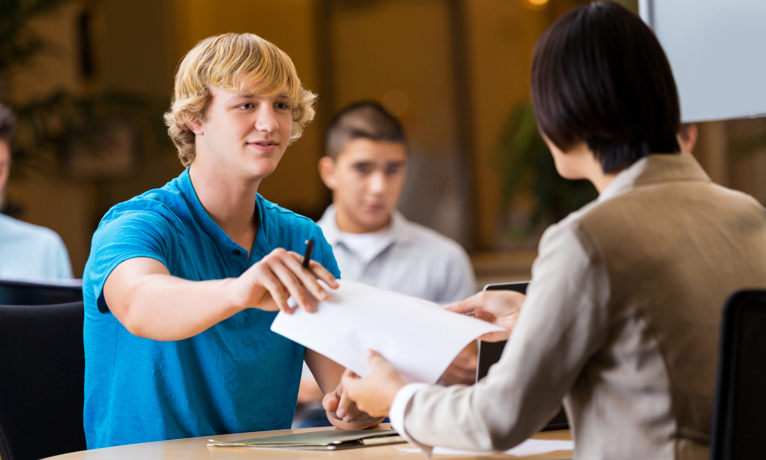 A picture of a young male handing a resume to someone.