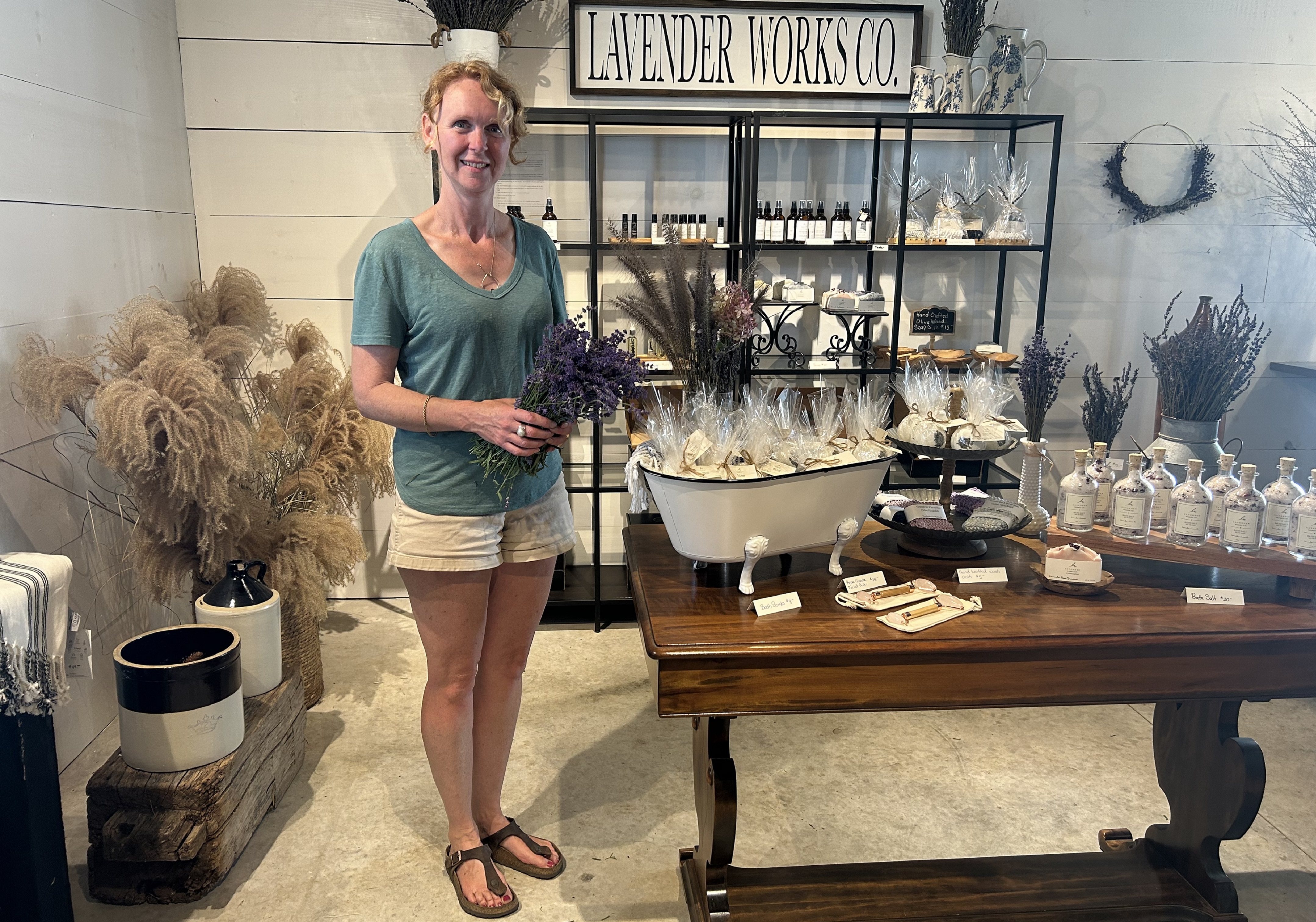 A picture of the owner of Lavender Works Co standing beside some of her lavender products.
