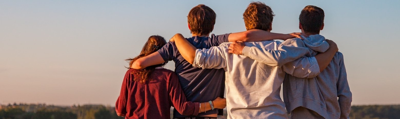 Four teenagers with arms over each others shoulders  standing in farmers field 