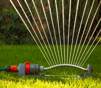 Lawn Sprinkler spraying water on green grass lawn