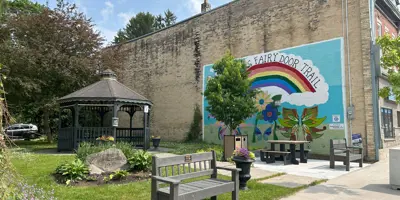 [A gazebo, benches and accessible picnic table in a park with a mural on the building wall in the background.] 